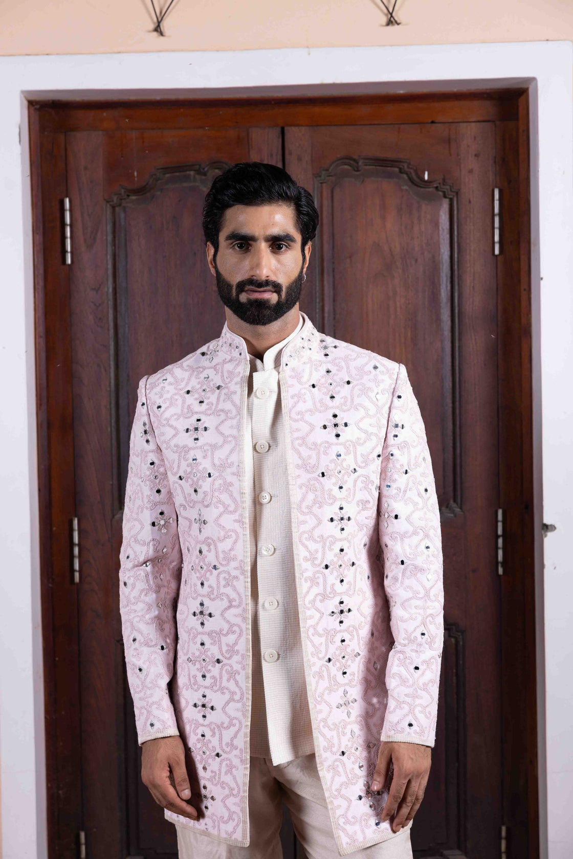 Soft pink tussar silk long jacket with mughal jali inspired resham, kasab and mirror work paired with ivory textured tissue sleeveless button bundi and flared pant Nafsstore